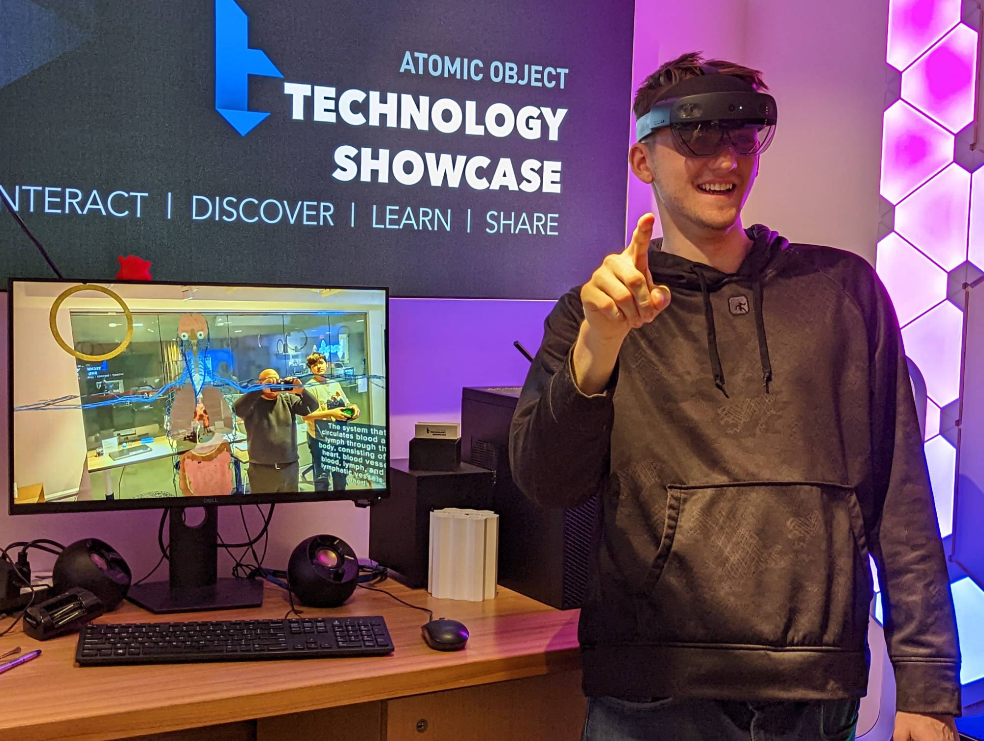 Student uses Hololens 2, his point of view is displayed next to him on a monitor.